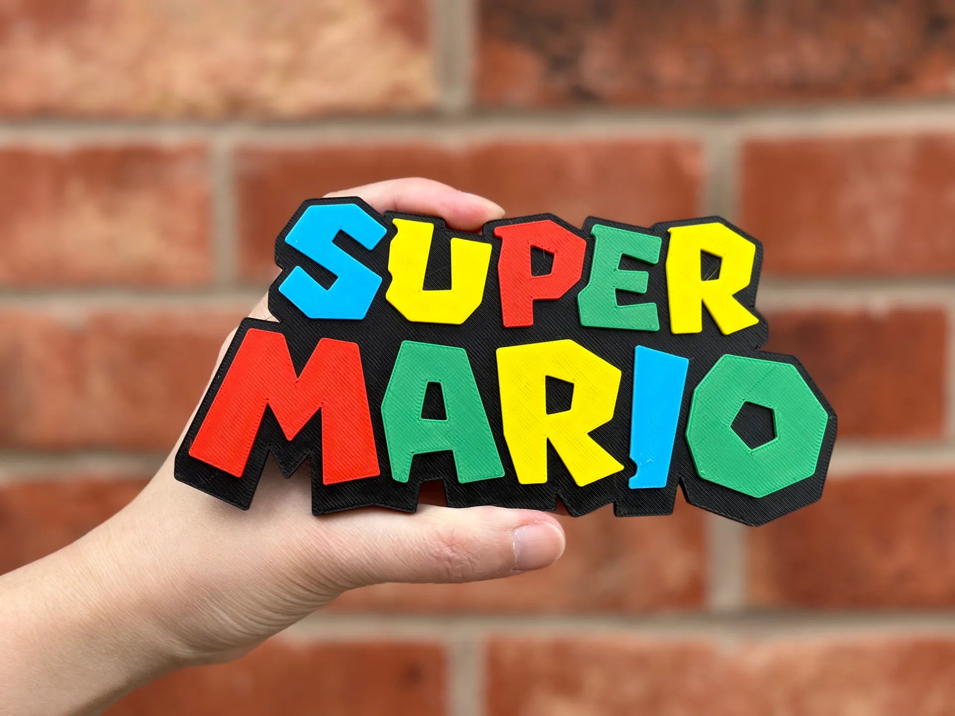 Logo 3D de Super Mario con acabado mate y gran nivel de detalle para decoración de vitrinas, escritorios y zonas gaming.