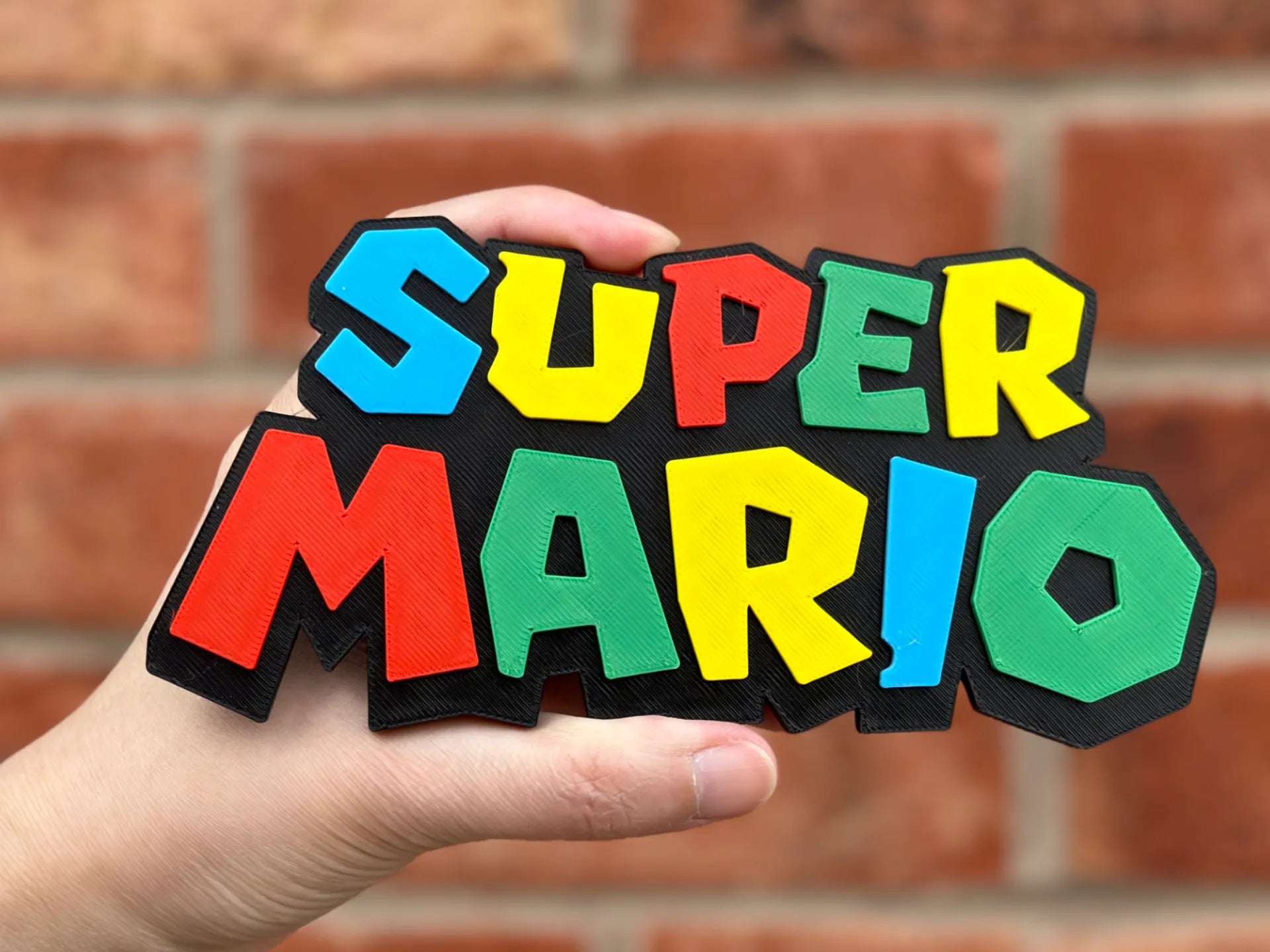 Logo 3D de Super Mario con acabado mate y gran nivel de detalle para decoración de vitrinas, escritorios y zonas gaming.